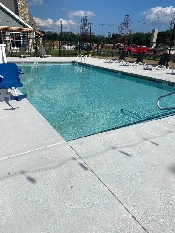 Finished pool with a light concrete deck, lounge chairs and a blue pool lift