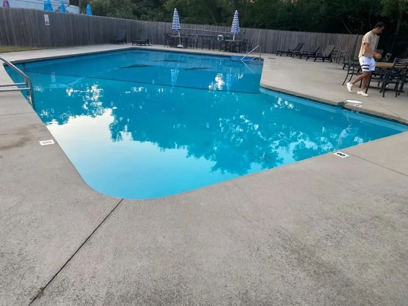 Large blue pool reflecting the trees, with lounge chairs and umbrellas behind a wooden fence