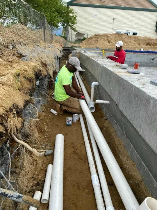 Crew member laying white PVC pipe in a trench beside a new pool shell