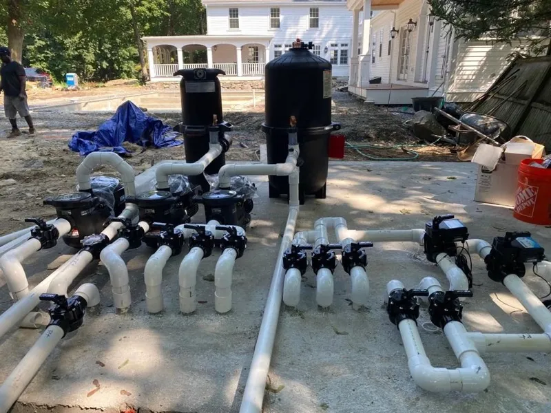 Filters, pumps and white PVC plumbing laid out on a slab before installation