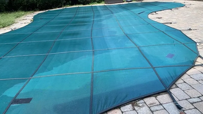 Green mesh safety cover stretched over a pool on a paver patio
