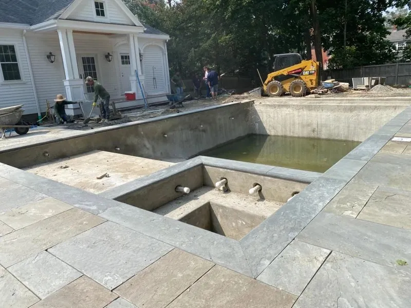 Crew working around a poured pool and spa shell with a skid steer in the background