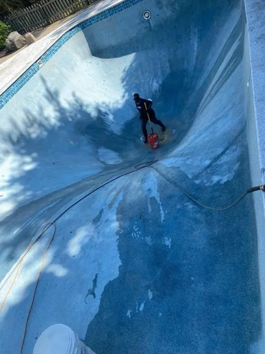 Worker cleaning the blue tiled surface of a drained pool