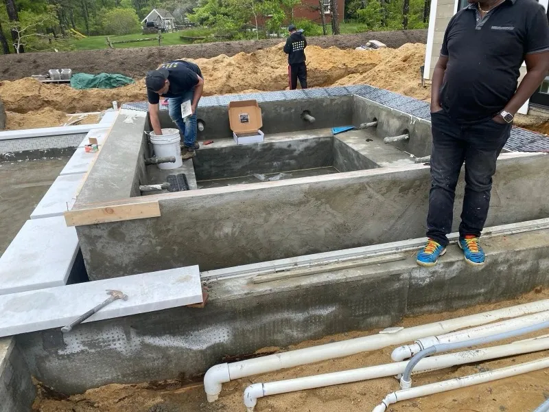 Concrete pool and spa shell under construction with plumbing lines in the foreground