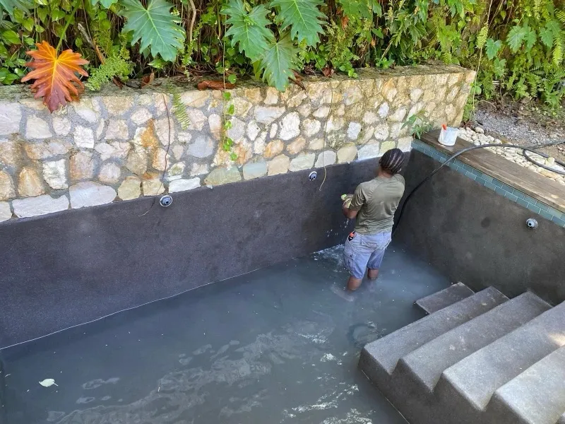Worker inside a pool with dark plaster walls, steps and a natural stone retaining wall
